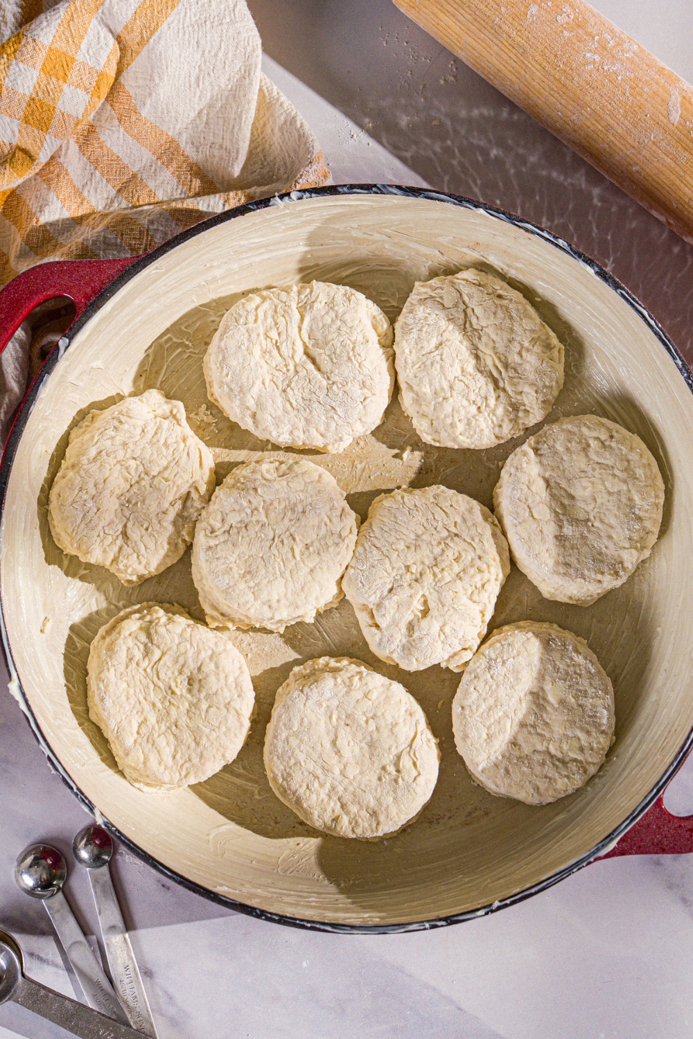 A baking dish with unbaked Hardee's biscuit dough pieces. The dish is on a marble counter with a yellow checkered napkin.