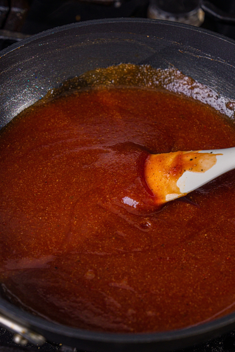 A skillet with a rubber spoon stirring a homemade BBQ sauce mixture.