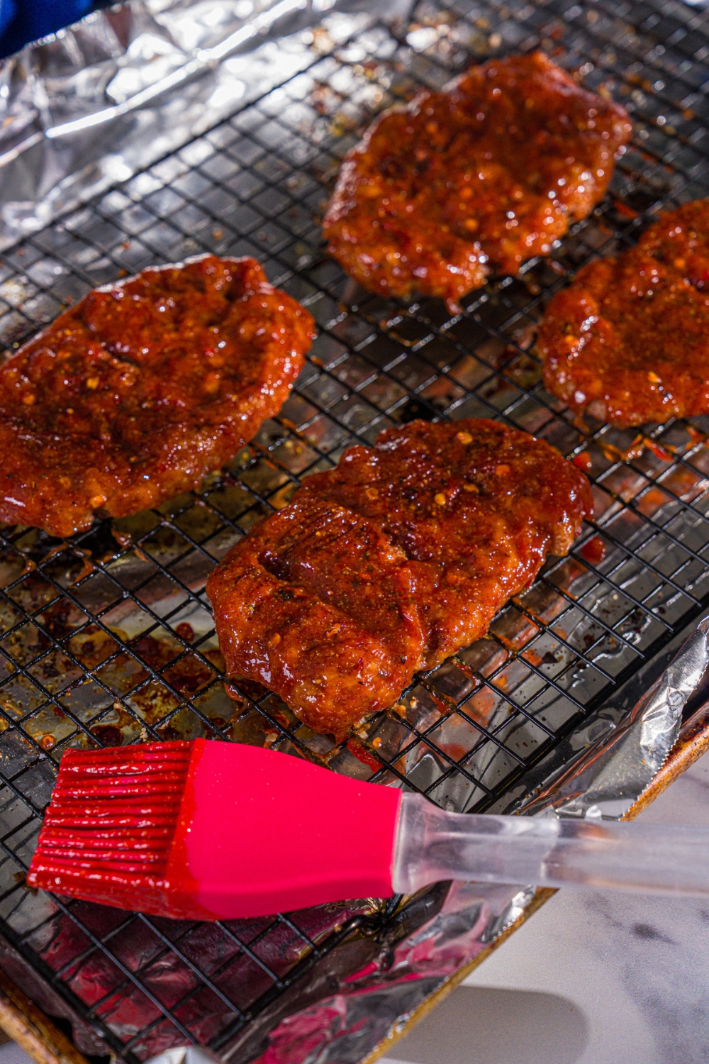 Baked seasoned McRib patties brushed with homemade BBQ sauce on a wire rack over a baking sheet lined with foil.