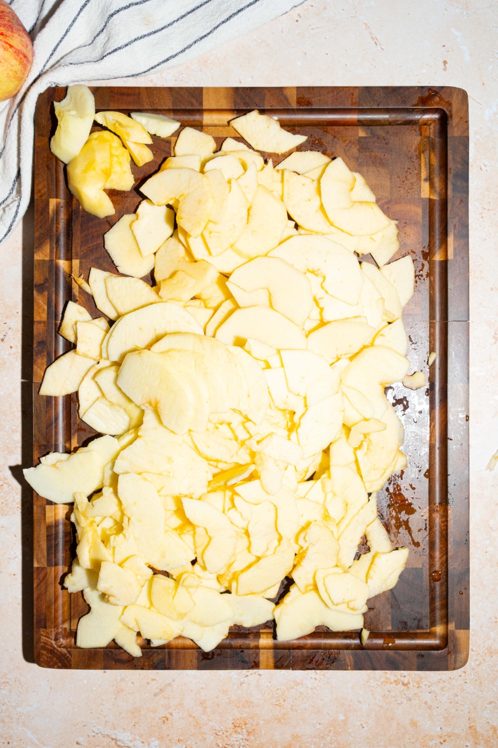 A wooden board with sliced apples. The board is on a tan counter with a white striped napkin.