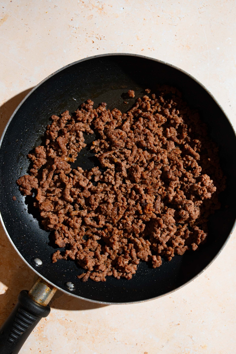 A skillet with cooked ground beef. The skillet is on a tan counter.