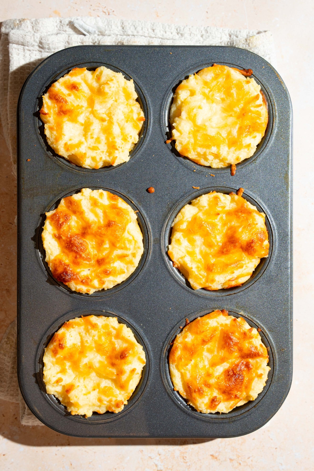 A muffin tin with baked mashed potato cups. The tin is on a tan counter.