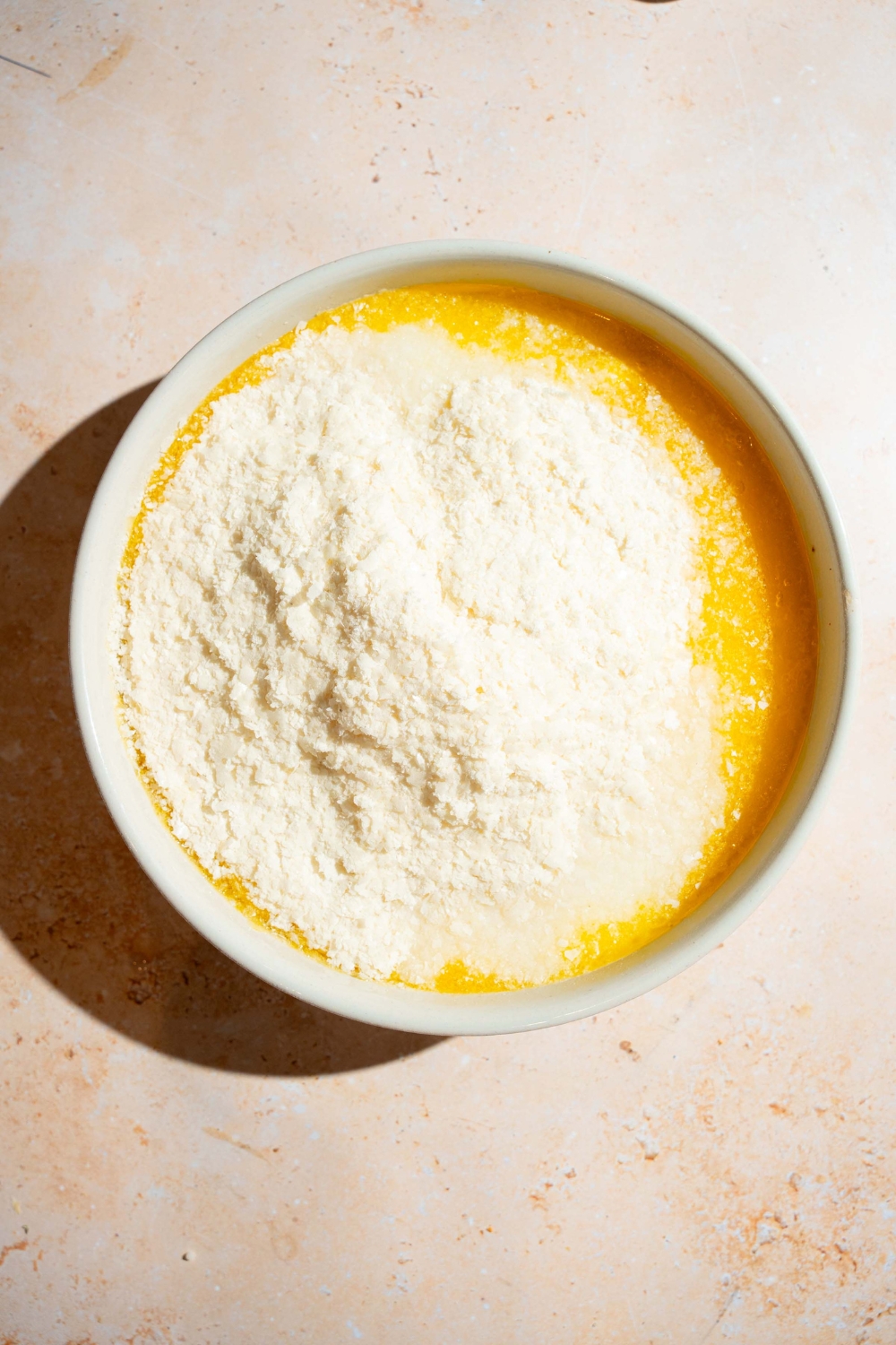 A large bowl with a butter and milk mixture topped with instant mashed potato mix. The bowl is on a tan counter.