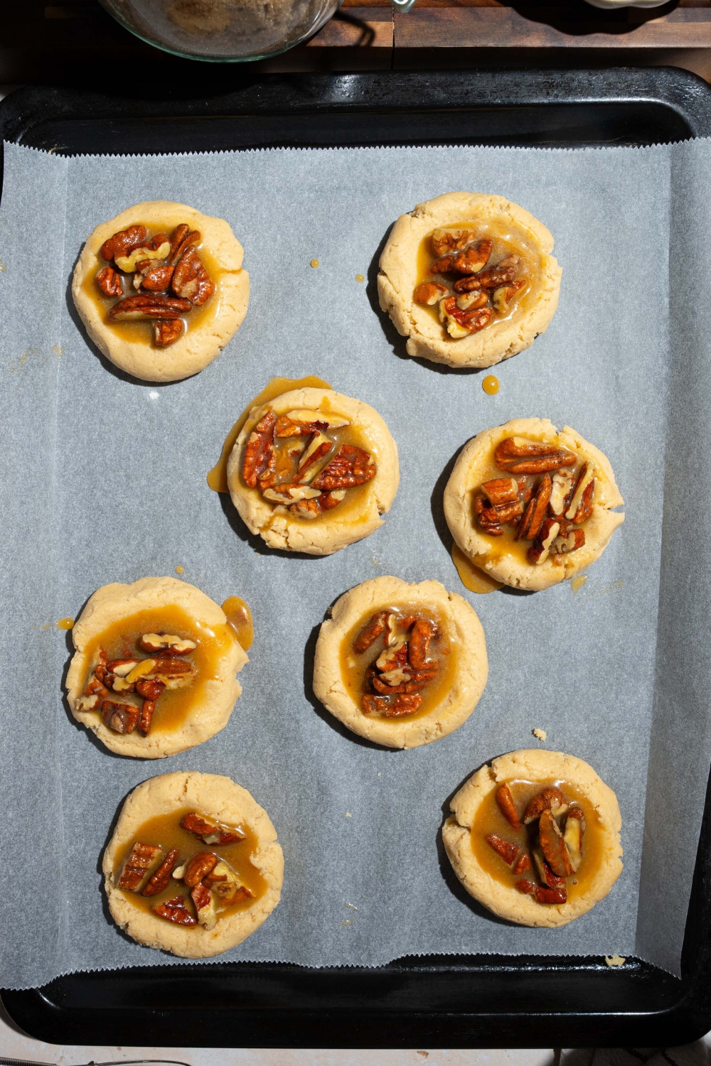 A baking sheet lined with parchment paper with unbaked pecan pie cookies.