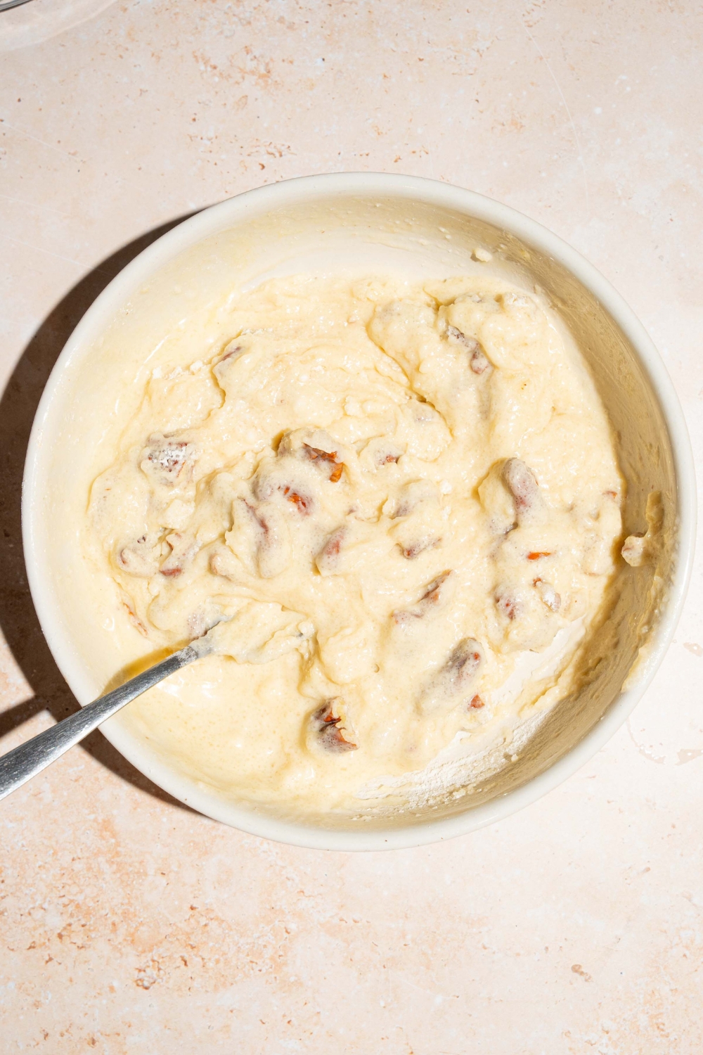 A large bowl with a pecan pie cobbler batter with a spoon in the bowl. The bowl is on a tan counter.