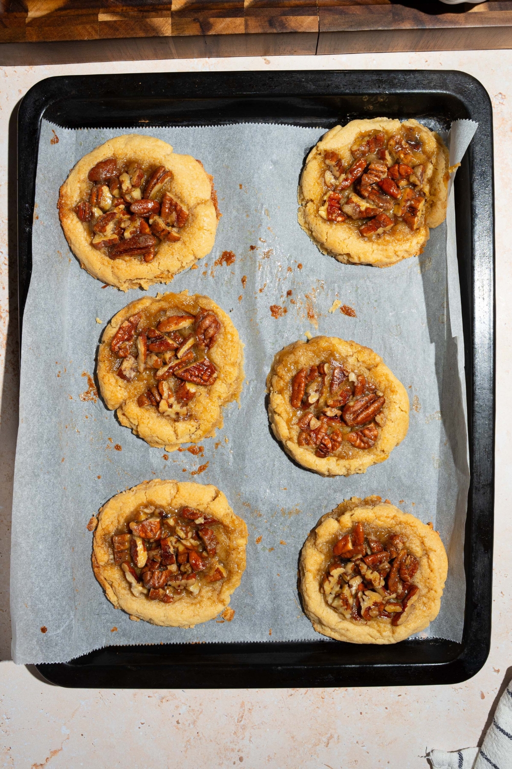 A baking sheet lined with parchment paper with baked pecan pie cookies. The sheet is on a tan counter.