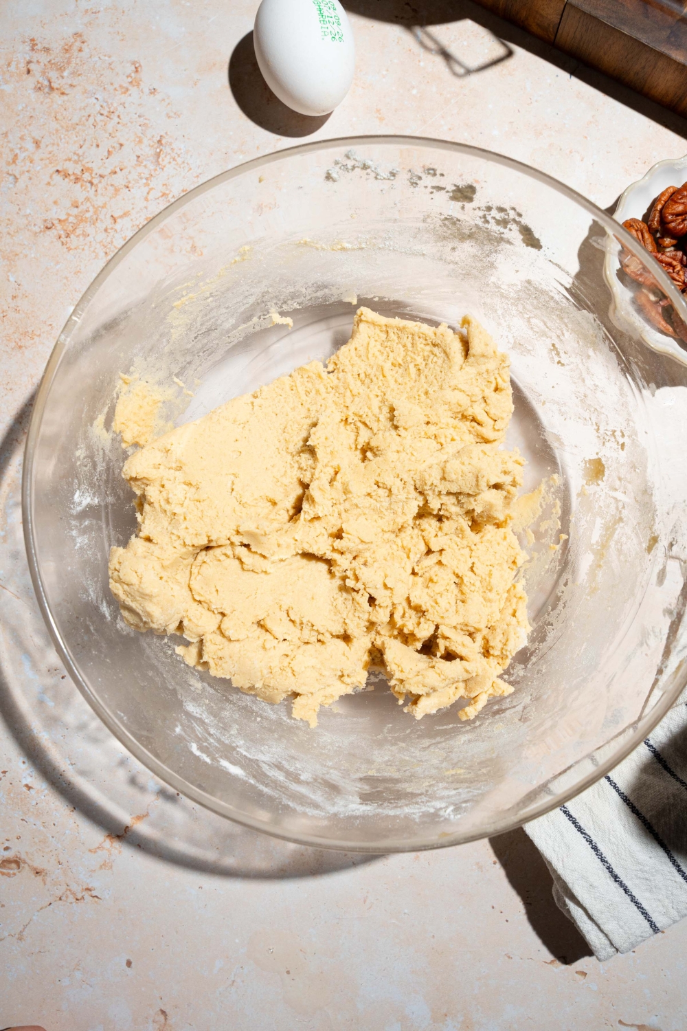 A large bowl with pecan pie cookie dough. The bowl is on a tan counter with an egg.