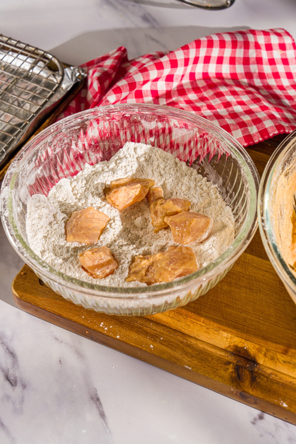 A bowl of dry mix with marinated chicken pieces. The bowl is on a wooden board with a red striped napkin.