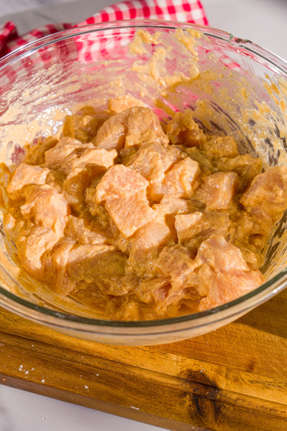 A bowl of marinated chicken pieces tossed with dry mix and egg. The bowl is on a wooden board.