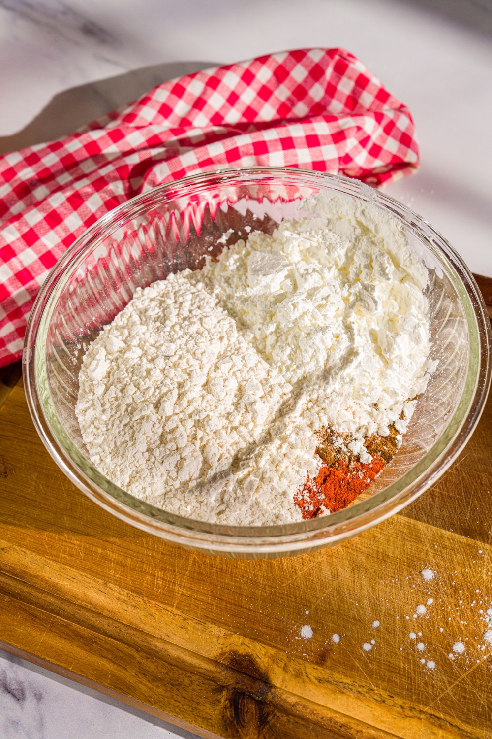 A bowl of dry mix ingredients including flour, cornstarch, garlic powder, onion powder, chili powder, and more. The bowl is on a wooden board.
