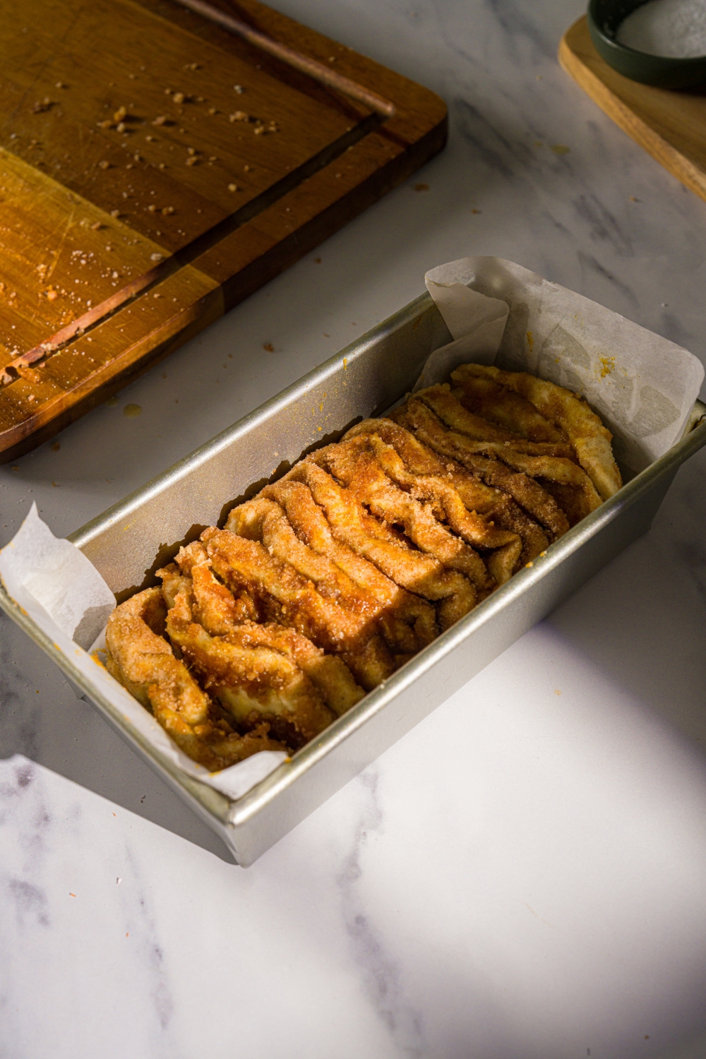 A loaf pan lined with parchment paper with unbaked pumpkin pull apart bread. The pan is on a marble counter with a wooden board.