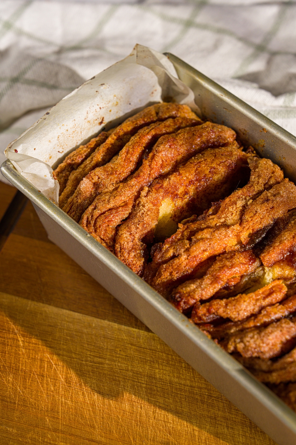 A loaf pan lined with parchment paper with baked pumpkin pull apart bread. The pan is on a wooden board with a white cloth napkin.