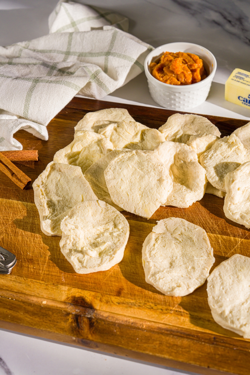 A wooden board with canned biscuits split in half. The board is on a marble counter with a small bowl of pumpkin puree and a white cloth napkin.