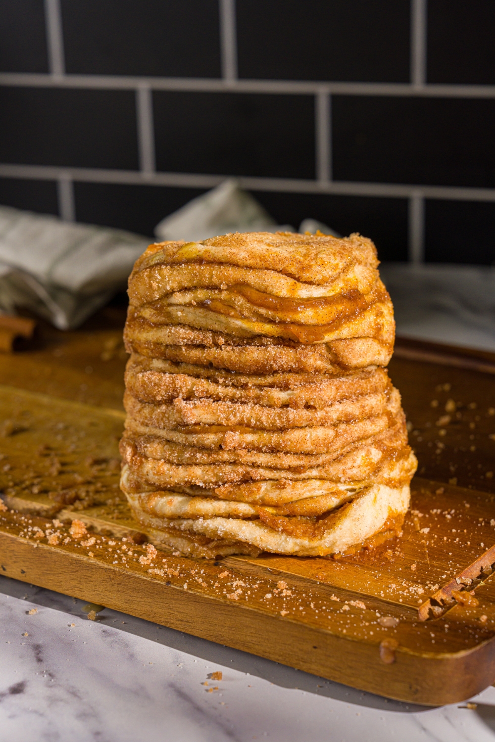 A stack of split canned biscuits layered with cinnamon sugar and pumpkin puree. The stack is on a wooden board.