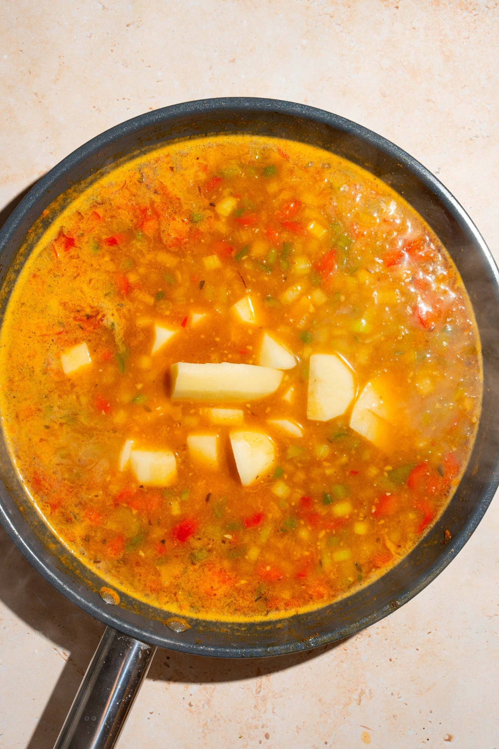 A skillet with sautéed vegetables in a broth mixture with potatoes. The skillet is on a tan counter.