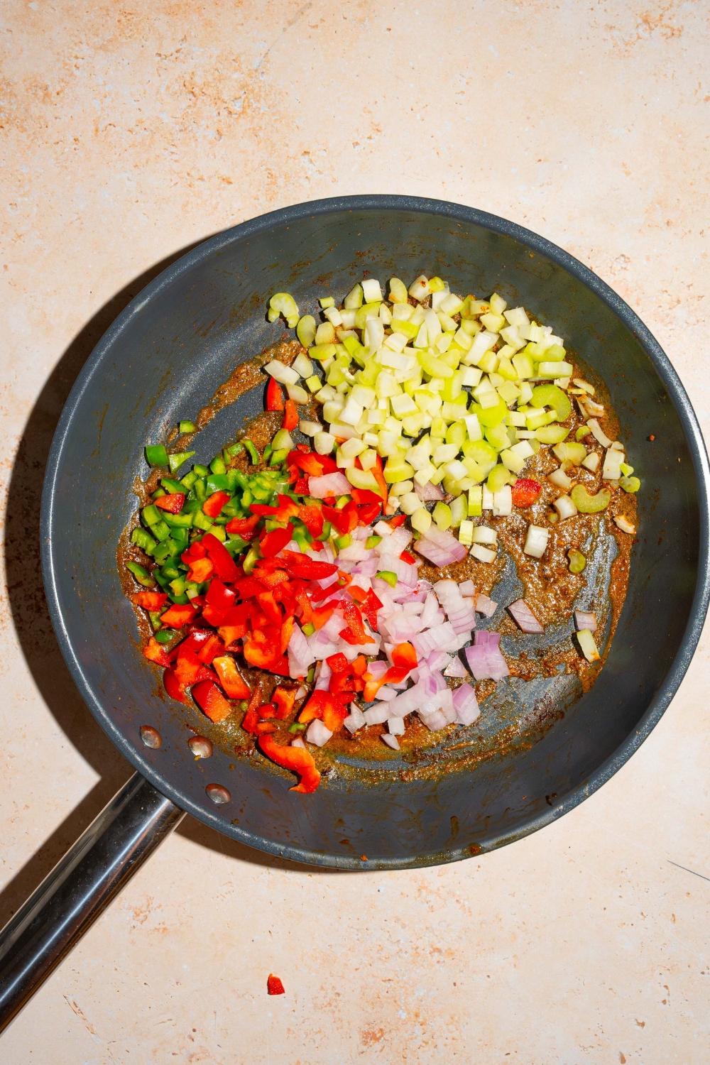 A skillet with chopped bell peppers, onions, and celery with a cajun seasoning mixture. The skillet is on a tan counter.