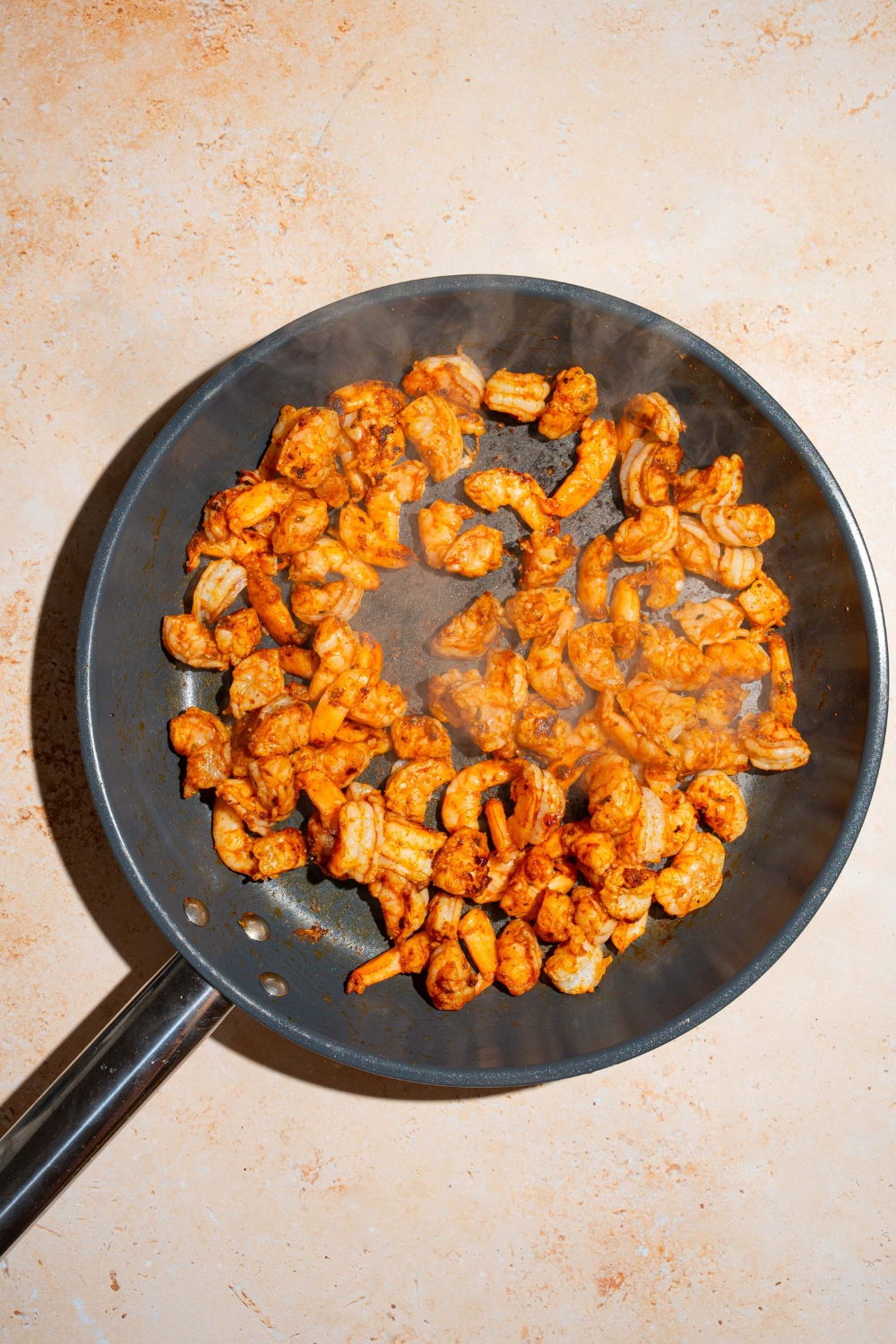 A skillet with browned seasoned shrimp. The skillet is on a tan counter.