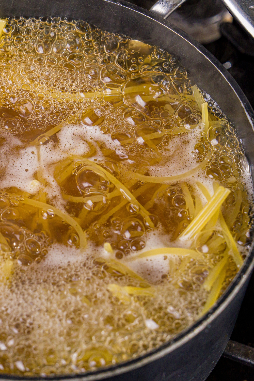 A large pot of boiling water cooking spaghetti. The pot is cooking on the stove.