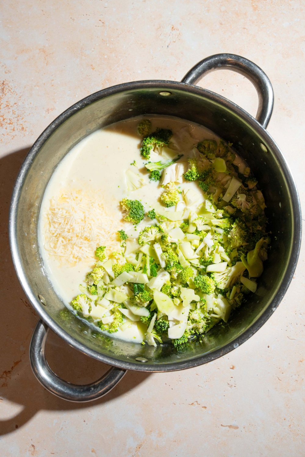 A large pot with a white cream sauce topped with shredded cheese and broccoli. The pot is on a tan counter.