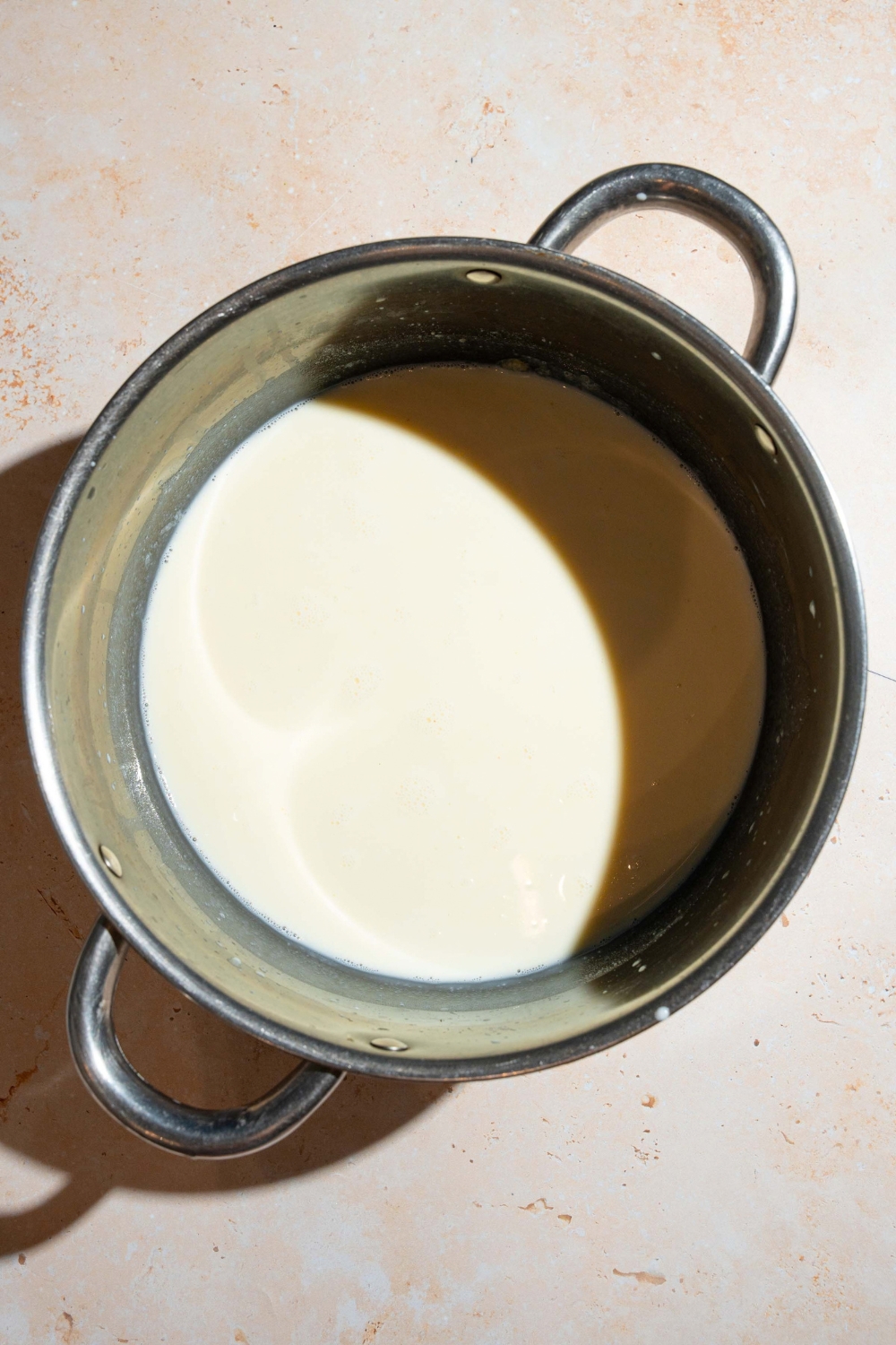 A large pot with a creamy white sauce base. The pot is on a tan counter.