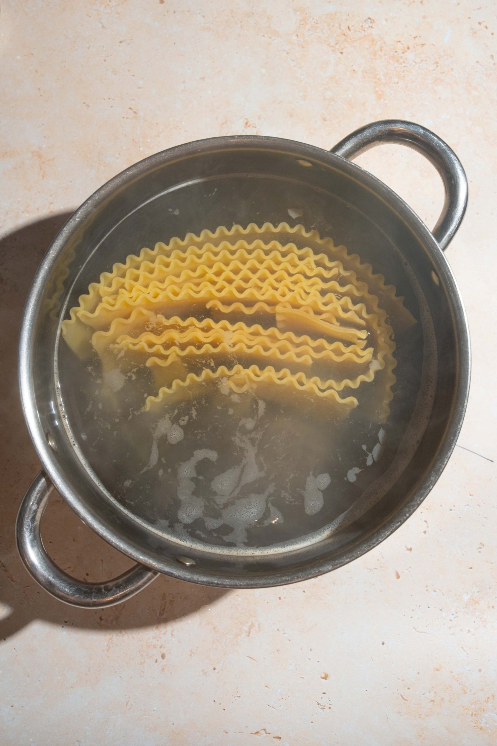 A large pot with lasagna noodles cooking in water. The pot is on a tan counter.