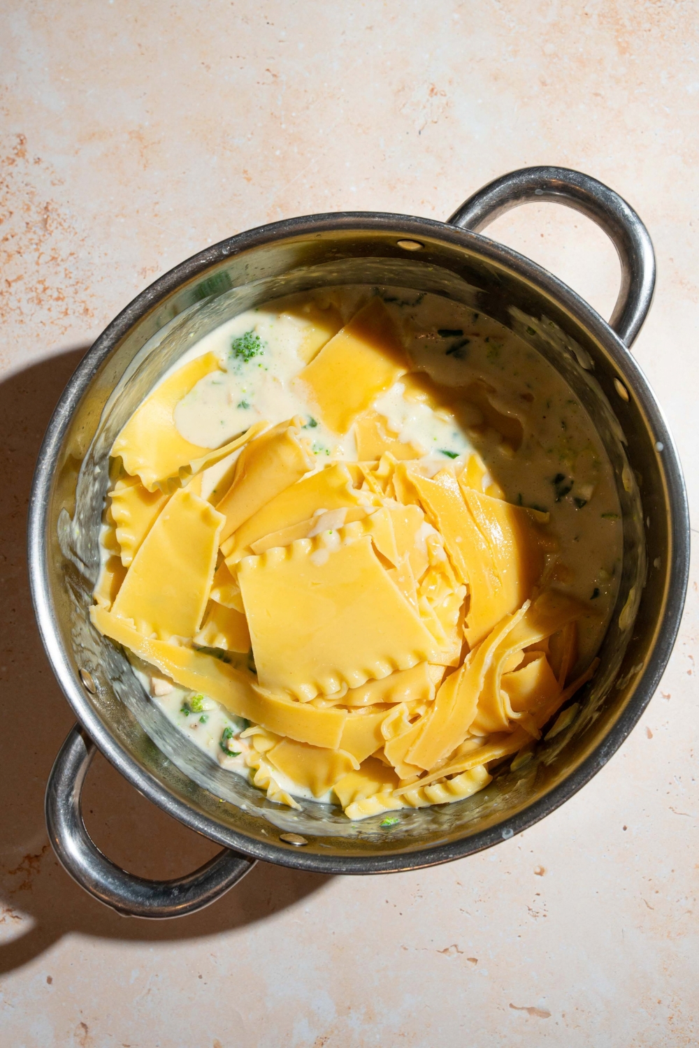 A large pot with chicken broccoli mixture topped with lasagna noodles. The pot is on a tan counter.