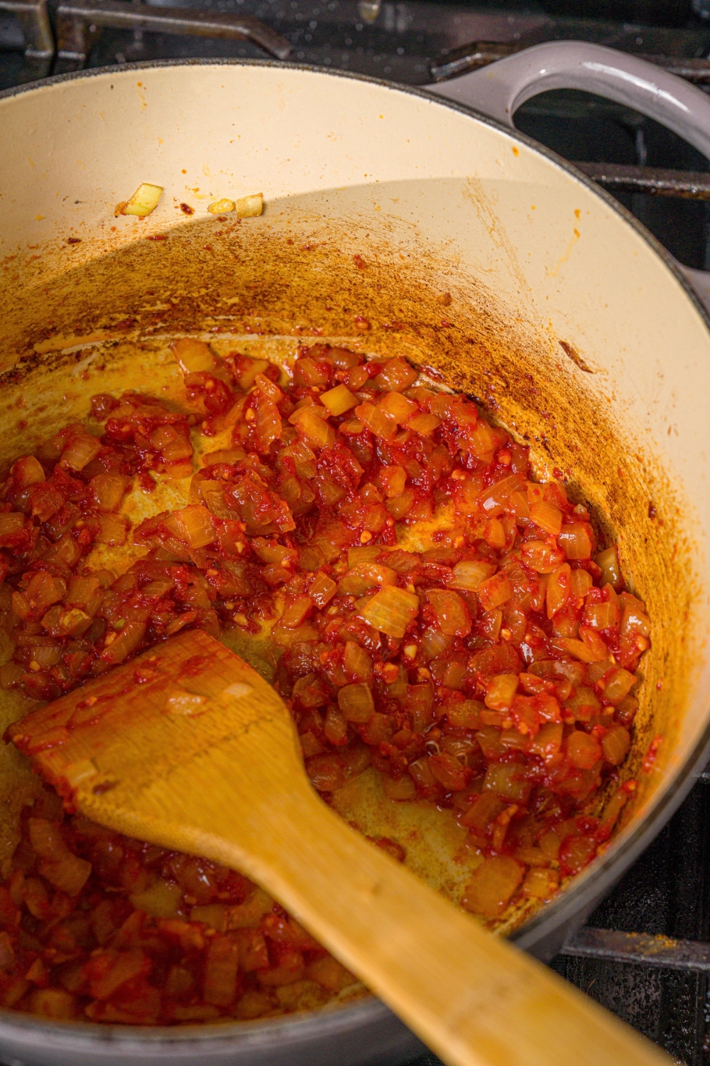 A pot with sautéed garlic, onion, and tomato paste. The pot is cooking on the stove.