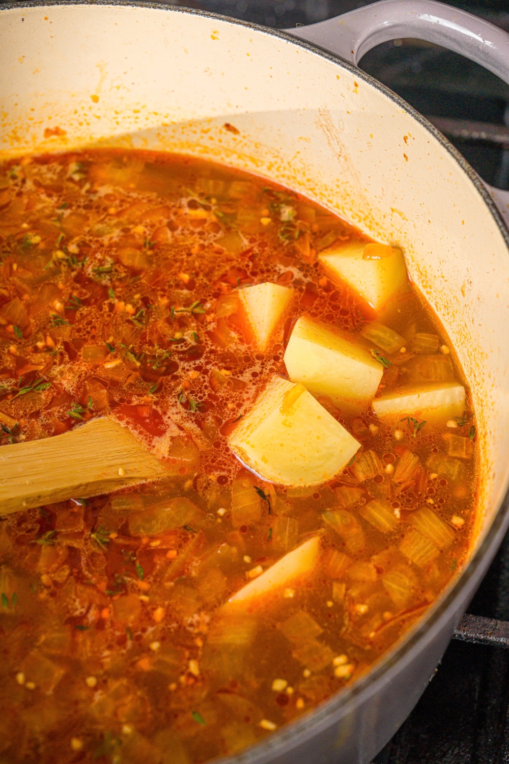 A large pot with shepherd's pie soup base with potatoes. A wooden spoon is stirring the mixture. The pot is cooking on the stove.
