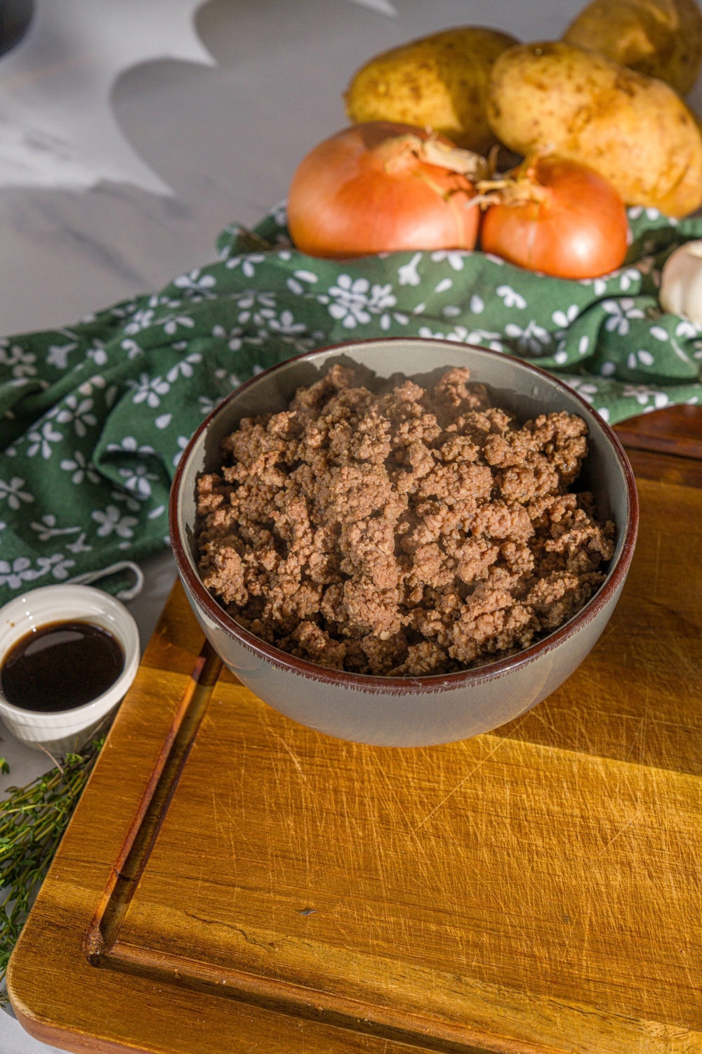 A bowl of browned ground beef on a wooden board with a green cloth napkin.