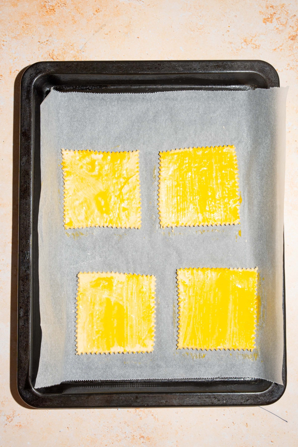 A baking sheet lined with parchment paper with four uncooked puff pastries brushed with egg wash. The sheet is on a tan counter.
