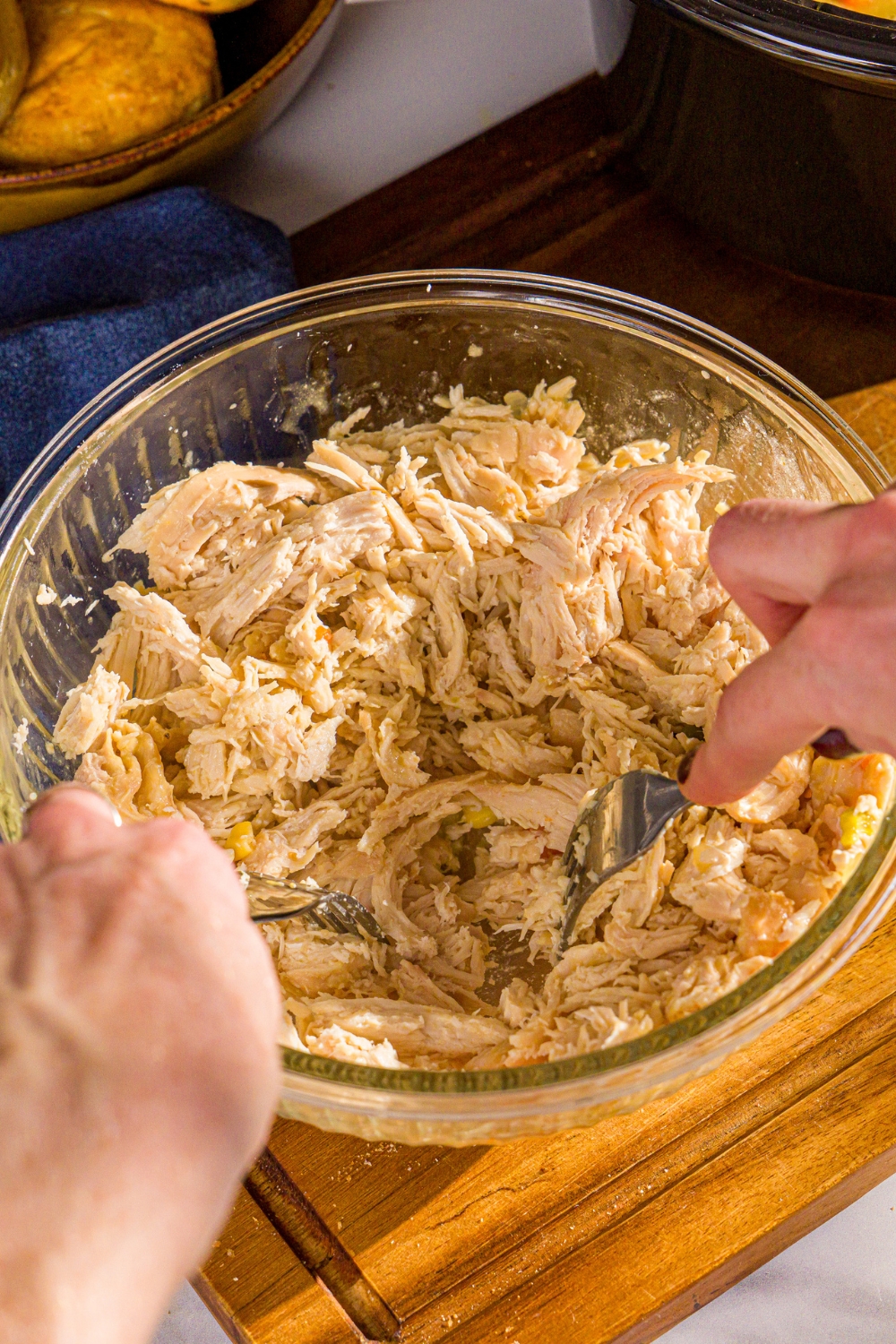 A bowl with two forks shredding chicken. The bowl is on a wooden board.