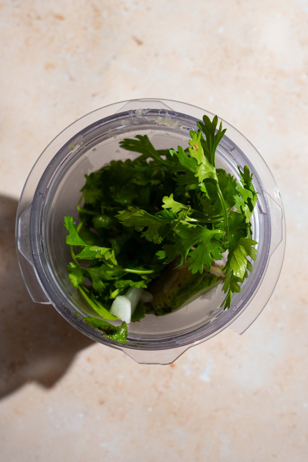 A blender jar with ingredients to make creamy avocado cilantro dressing. The jar is on a tan counter.