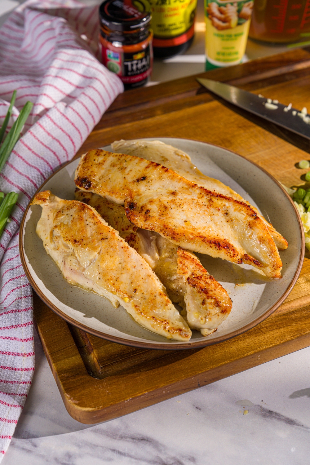 A plate with seared seasoned chicken breasts. The plate is on a wooden board.