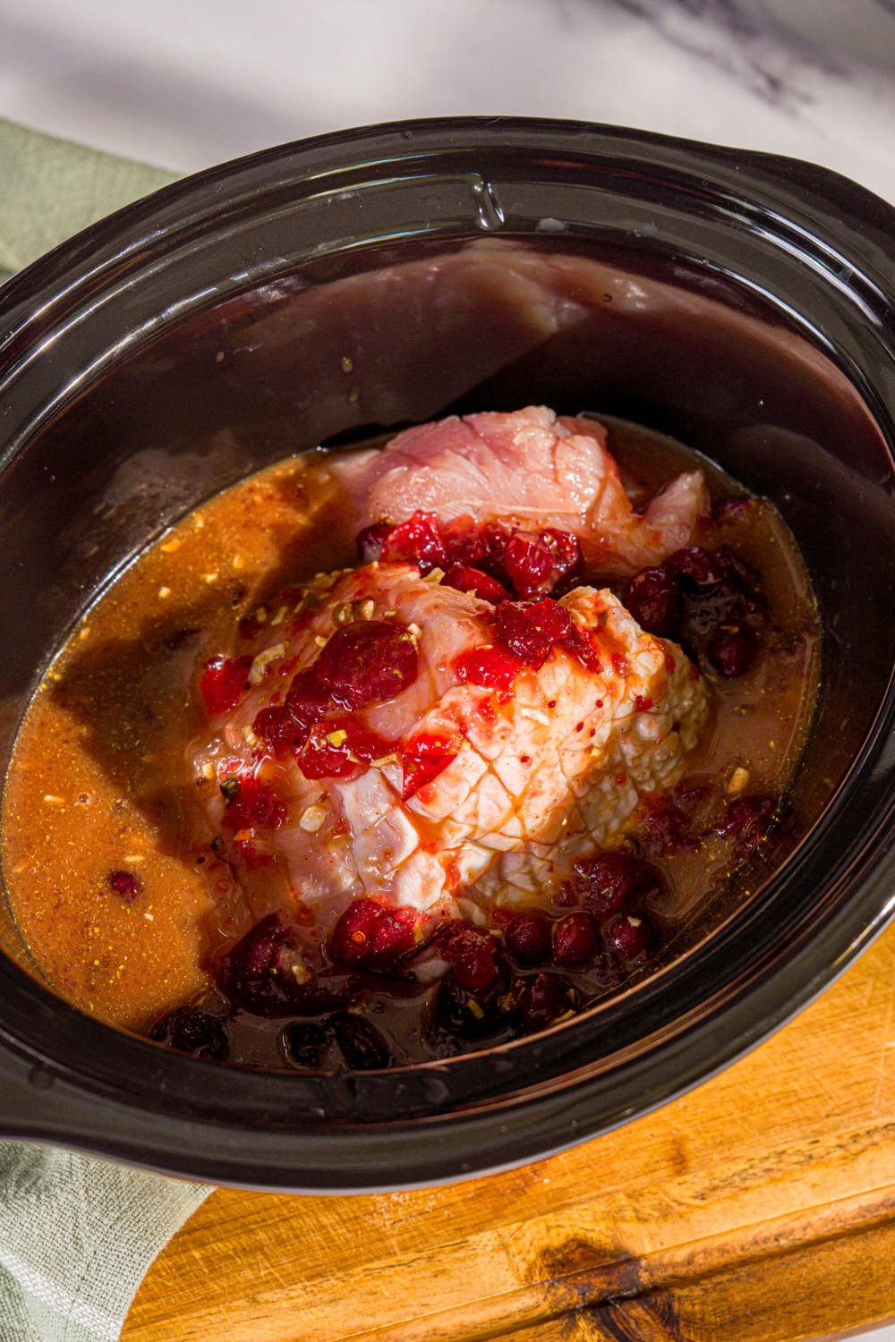 A crock pot with uncooked butterball turkey breast with cranberry sauce mixture. The crock pot is on a wooden board.