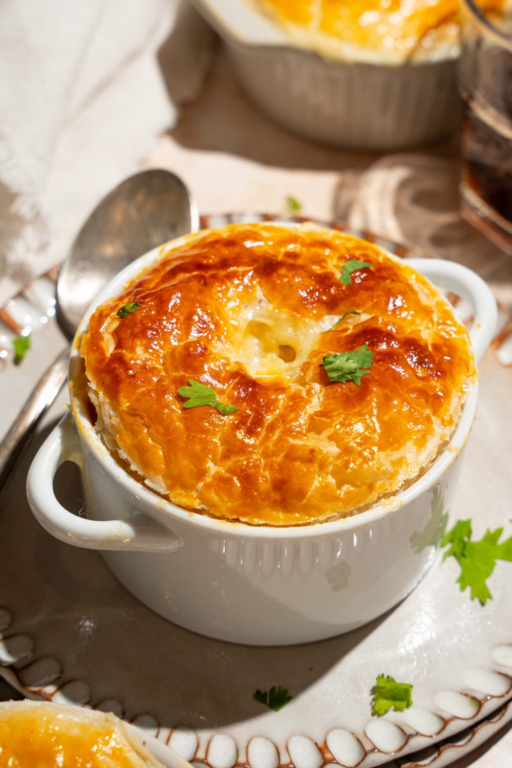 A small pie tin with baked KFC pot pie topped with puff pastry and garnished with fresh parsley. The tin is on plate with a spoon.