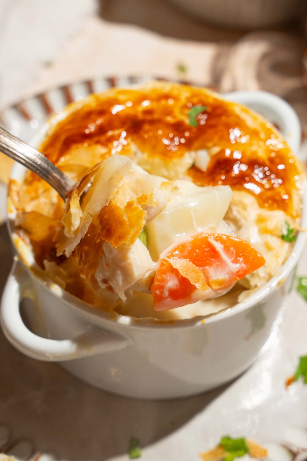 A small pie tin with baked KFC pot pie topped with puff pastry and garnished with fresh parsley. A spoon is taking a bite from the pot pie. The tin is on plate.