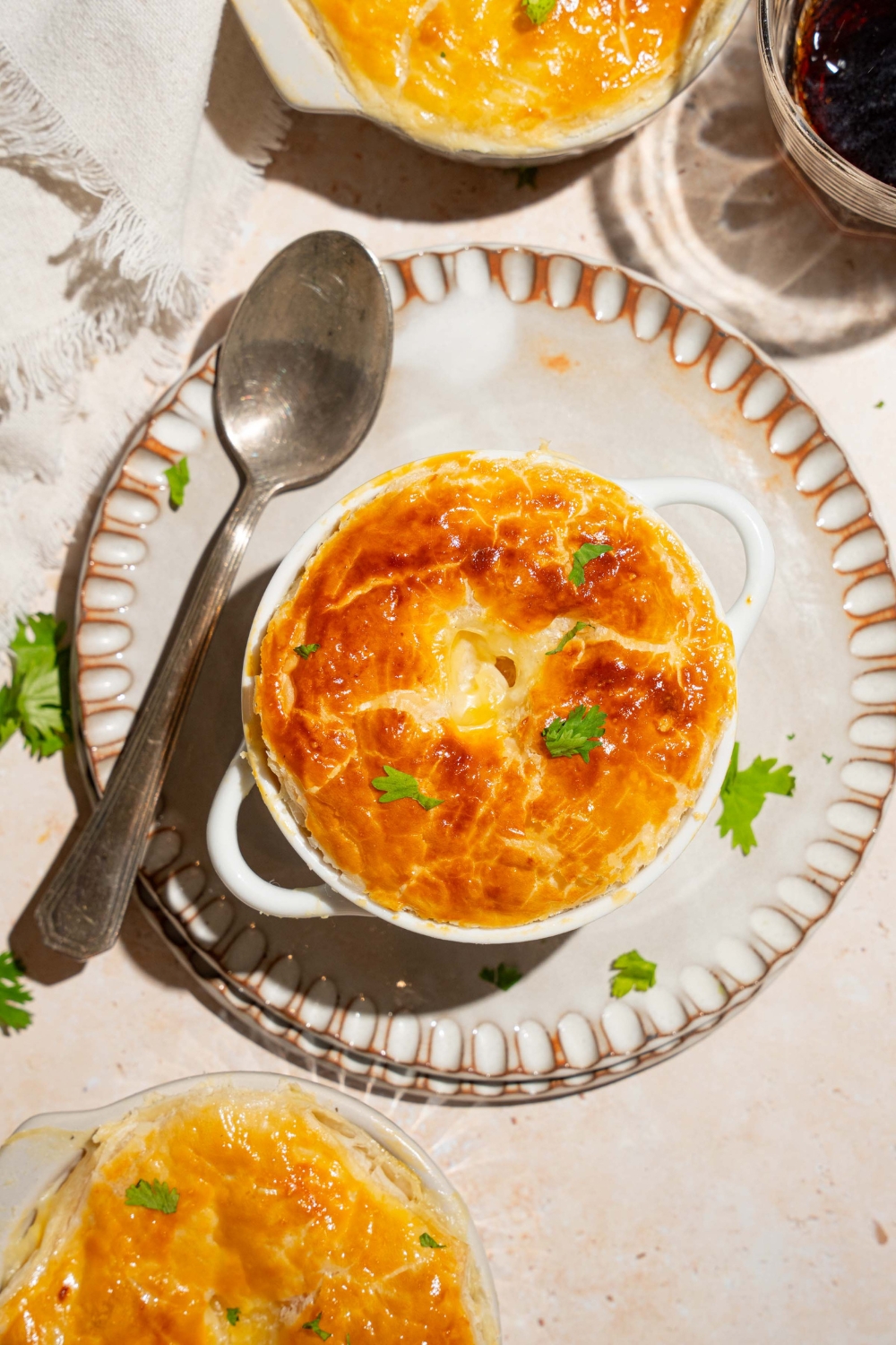 A small pie tin with baked KFC pot pie topped with puff pastry and garnished with fresh parsley. The tin is on plate with a spoon. The plate is on a tan counter with additional pot pies.