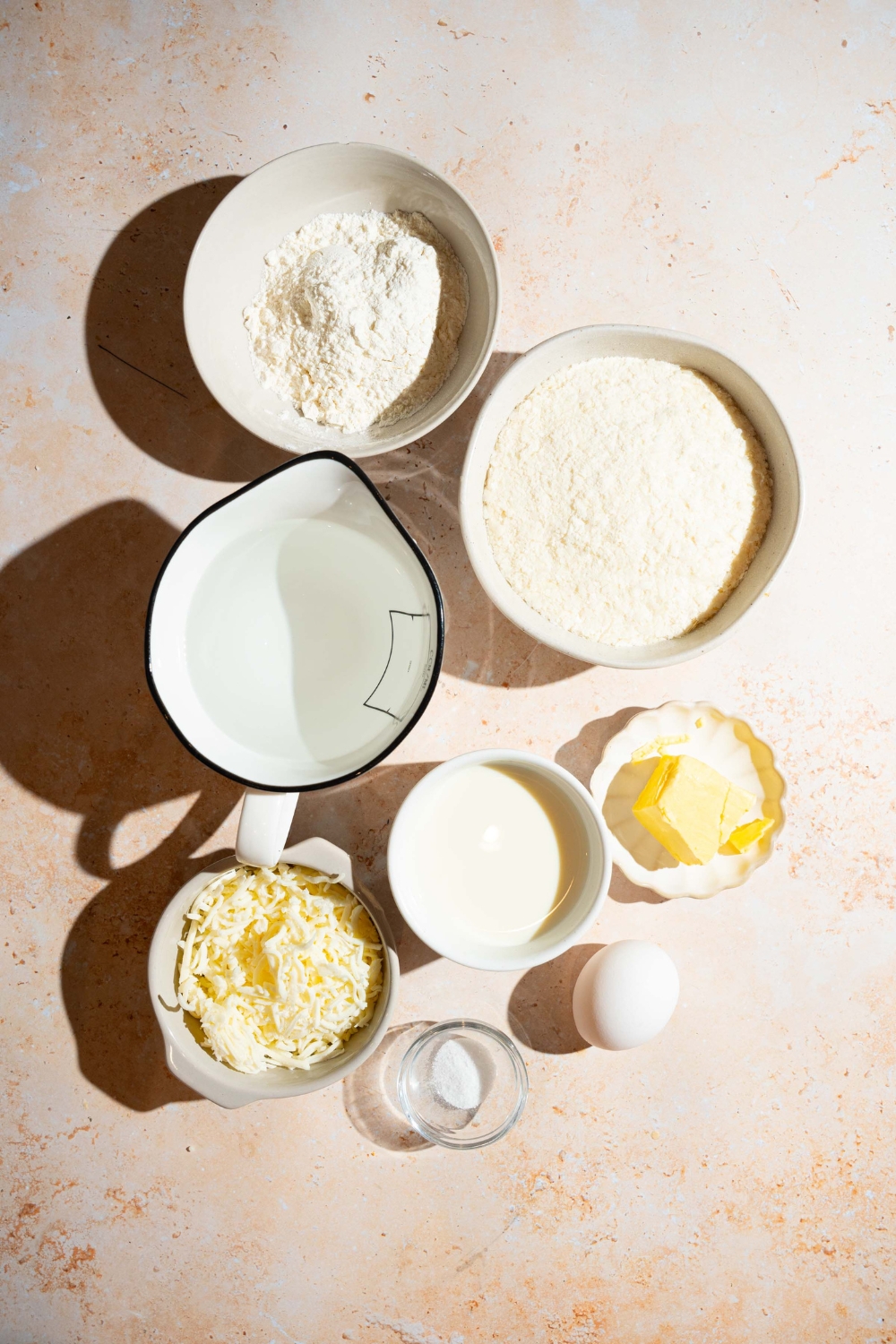 A tan counter with several bowls containing ingredients to make mashed potato cups including milk, egg, butter, instant mashed potatoes, water, and shredded cheese.