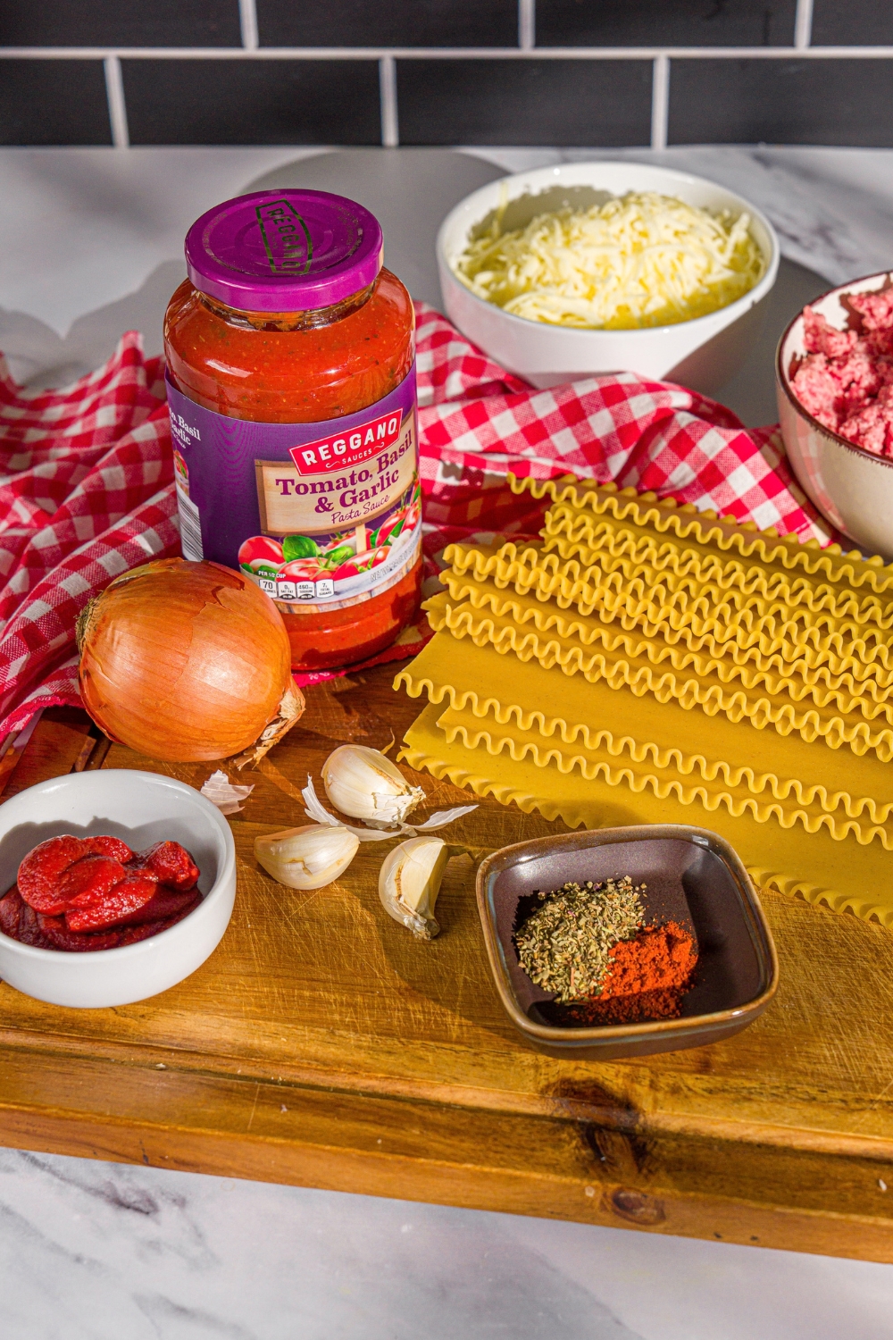 A wooden board with ingredients to make skillet lasagna including ground beef, lasagna noodles, tomato sauce, onion, garlic, tomato paste, cheese, and seasonings.