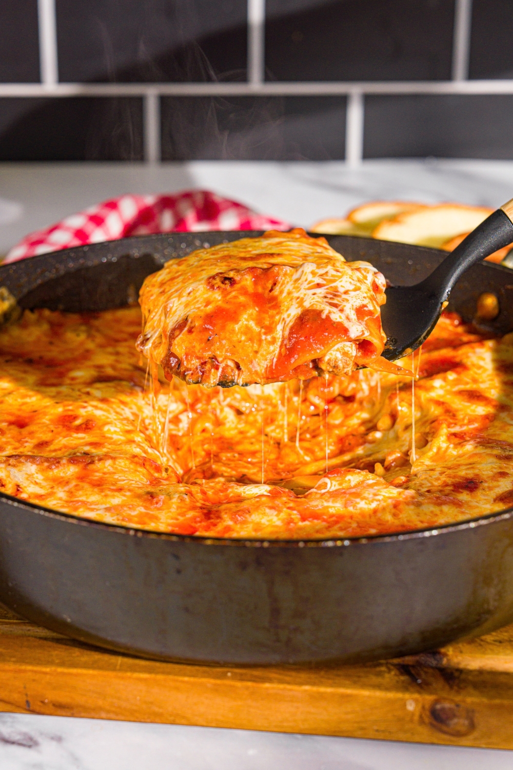 A spatula taking a slice of skillet lasagna from a skillet. The skillet is on a wooden board.
