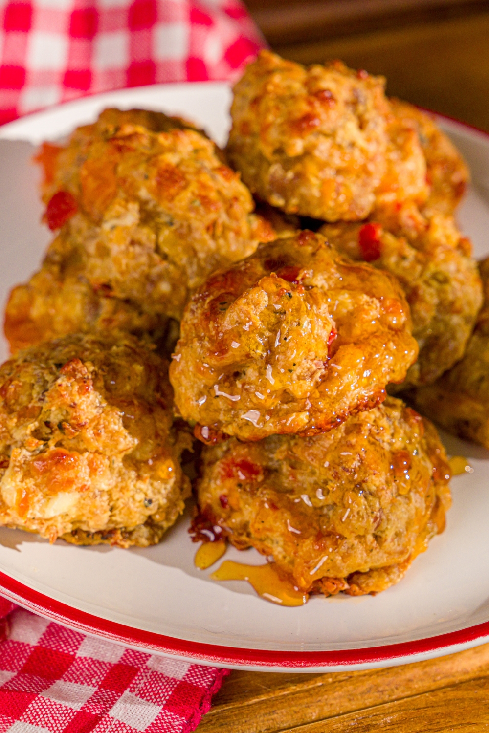 A plate of cheddar bay biscuit sausage balls drizzled with hot honey. The plate is on a wooden board with a red checkered napkin.