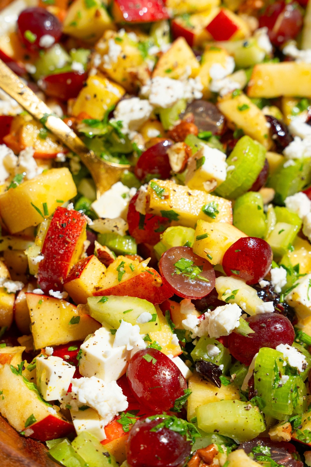 Apple crunch salad with apples, celery, pecans, feta cheese, parsley, and grapes tossed in a maple dijon dressing. There is a fork in the bowl.