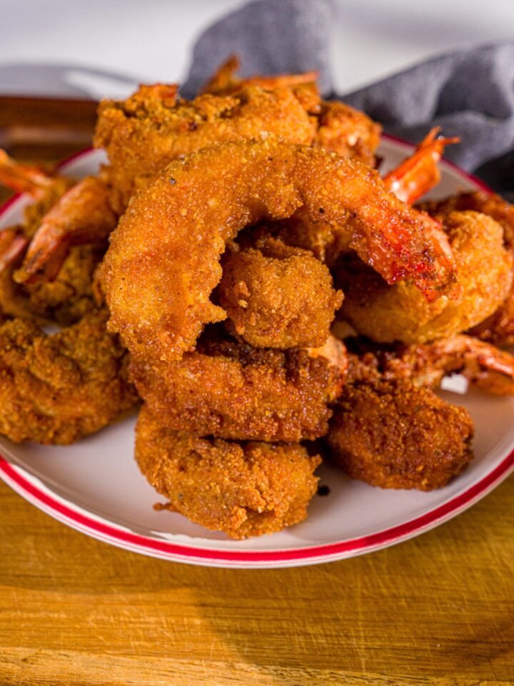 A plate of crispy fried prawns. The plate is on a wooden board with a blue cloth napkin.