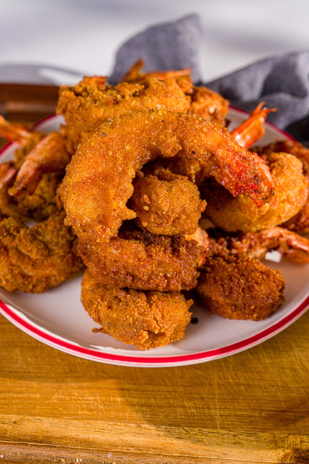 A plate of crispy fried prawns. The plate is on a wooden board with a blue cloth napkin.