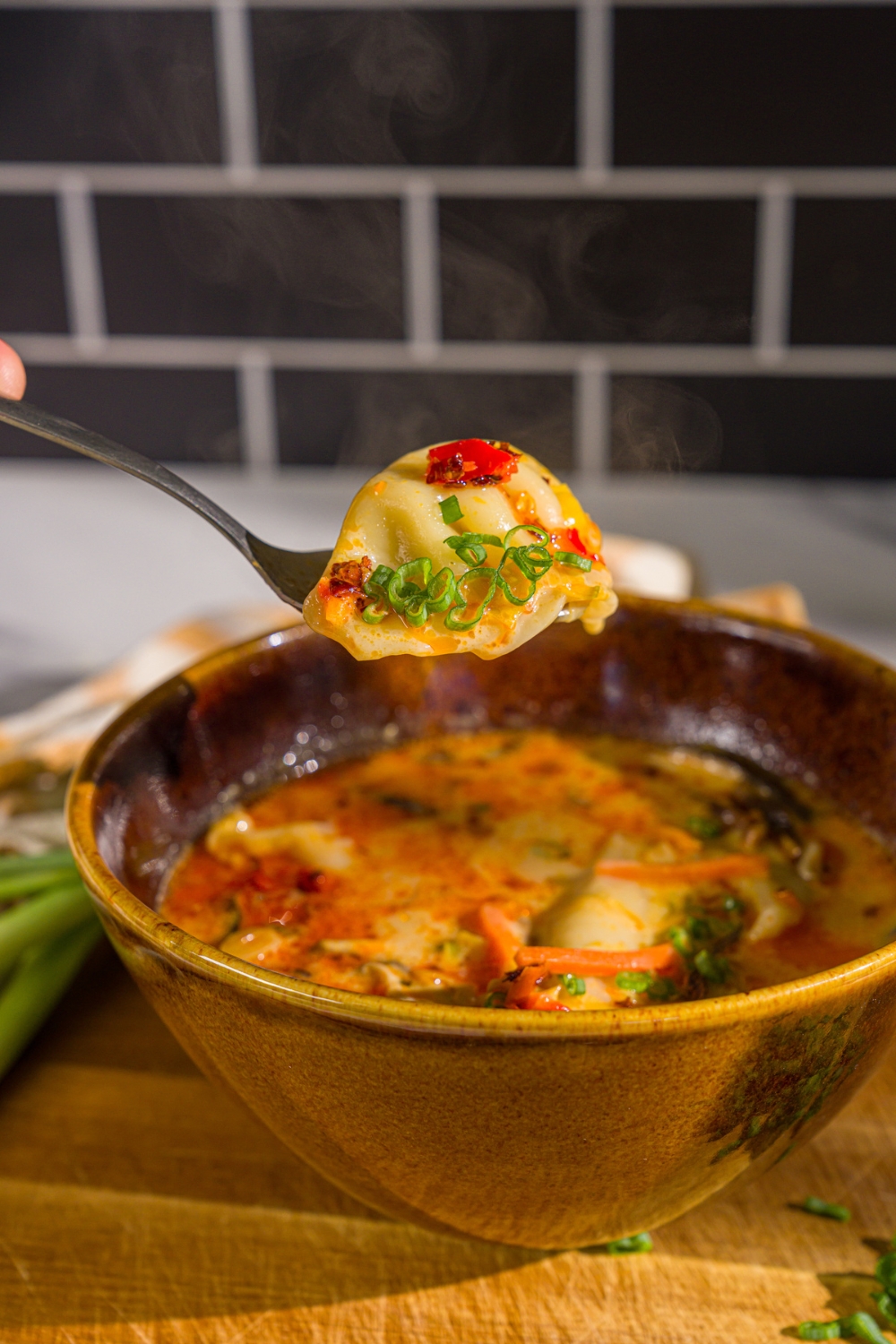 A close up of a spoon with a bite of creamy potsticker soup garnished with sliced green onion and chili crisp. There. is a bowl of soup blurred in the background.
