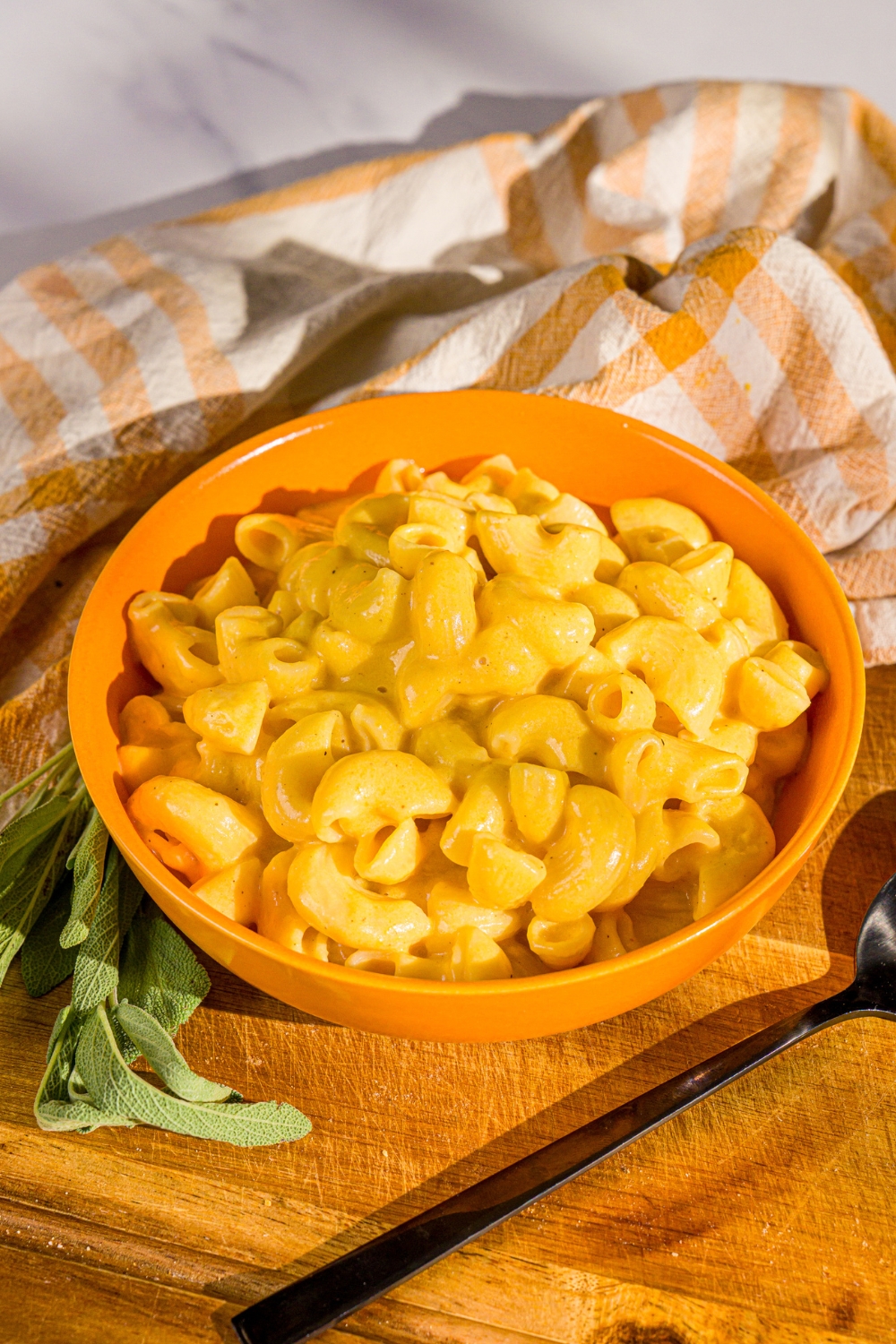 Butternut squash mac and cheese in an orange bowl that's on a wooden board.