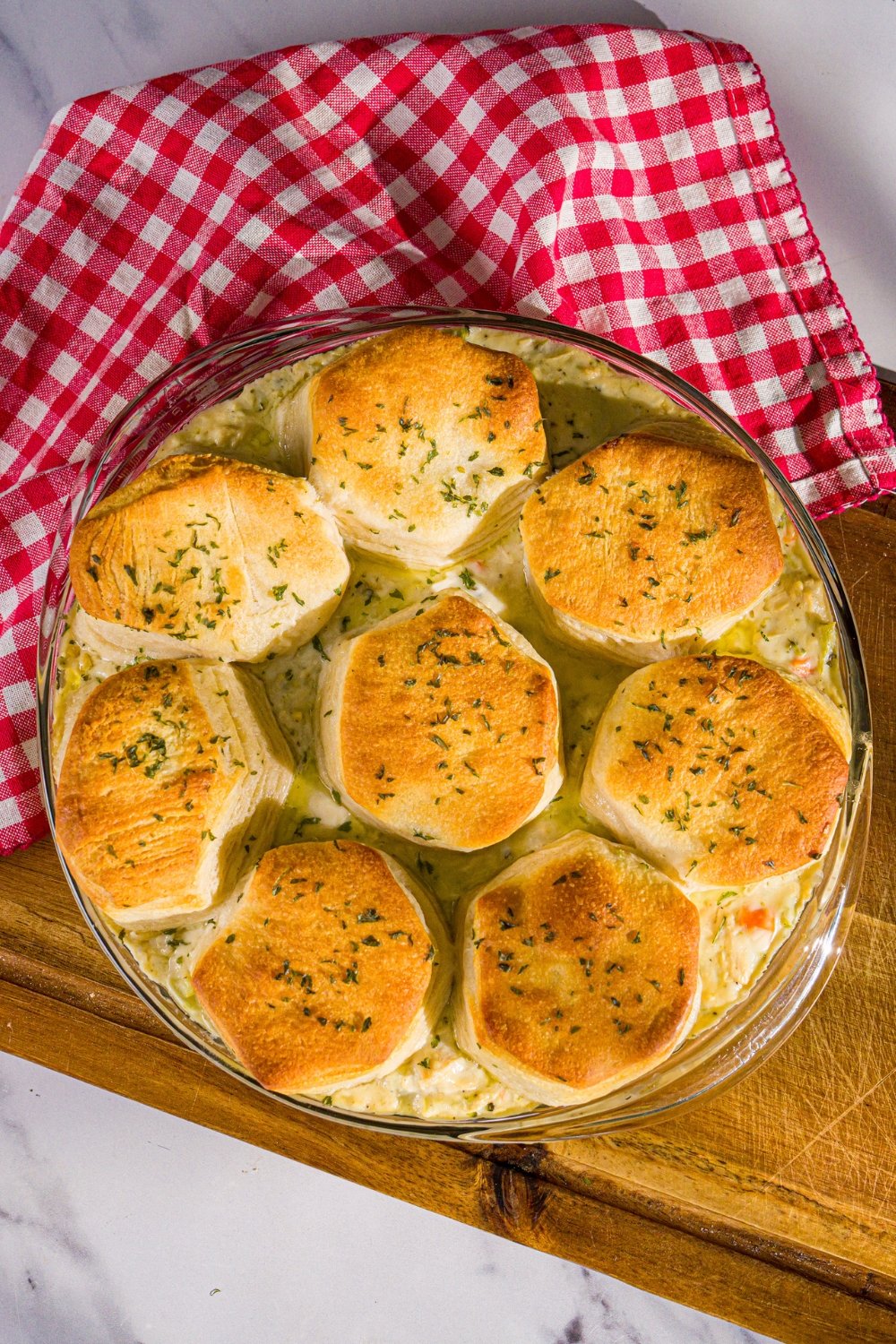 A round baking dish of Trader Joe's chicken pot pie with a biscuit topping. The dish is on a wooden board with a red checkered napkin.