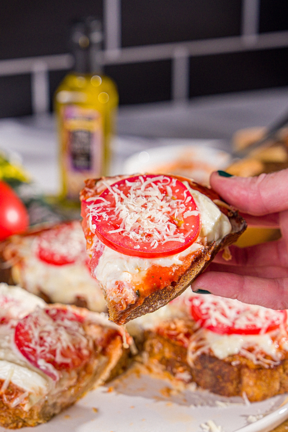 A close up of a slice of Hailey Bieber pizza toast topped with shredded parmesan. There is a plate of pizza toast blurred in the background.