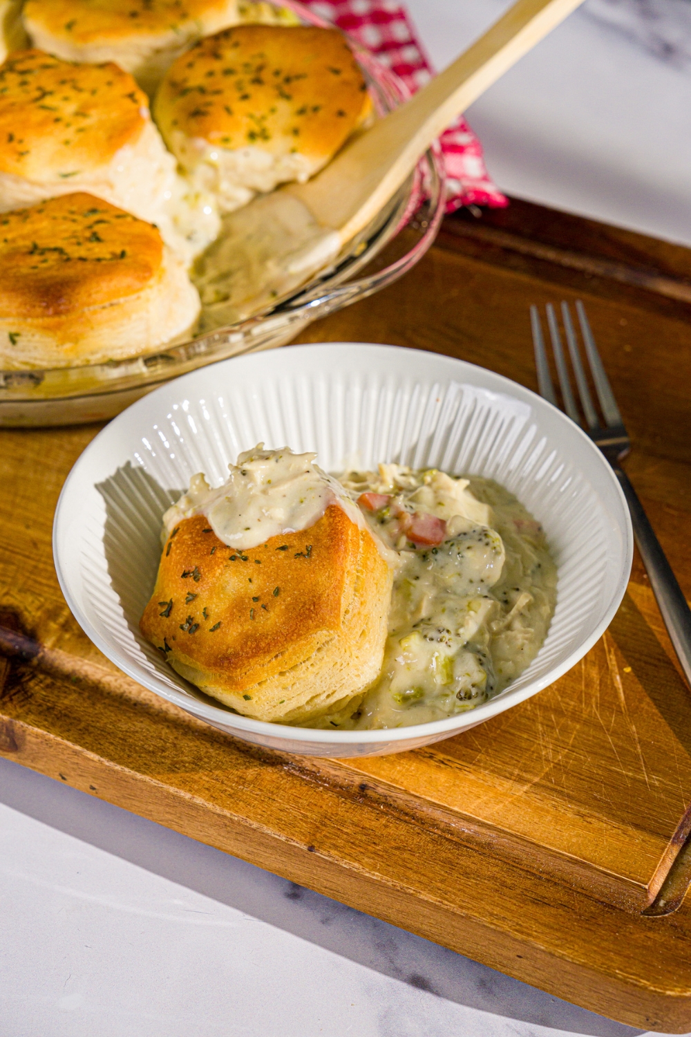 A bowl of Trader Joe's chicken pot pie with a biscuit topping. The bowl is on a wooden board with a fork and dish of pot pie.