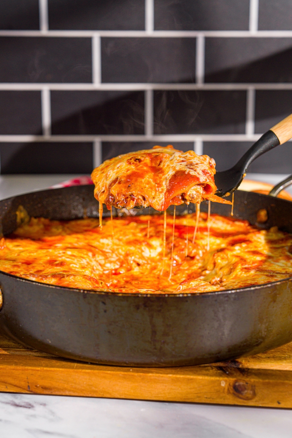 A spatula taking a slice of skillet lasagna from a skillet. The skillet is on a wooden board.